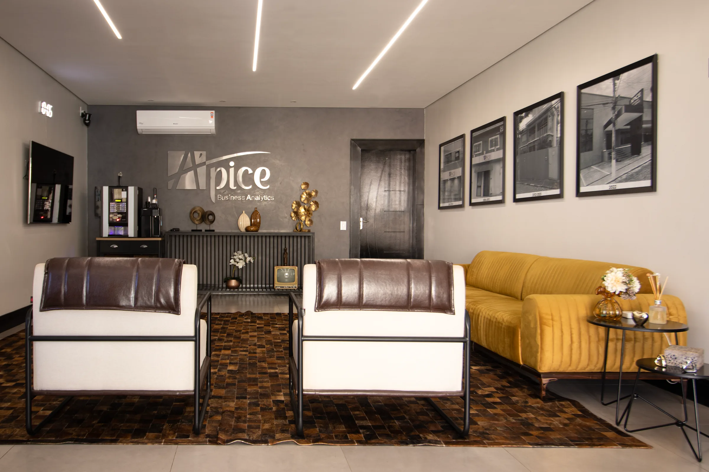 Recepção da Apice, com poltronas, sofá amarelo e a marca na parede.