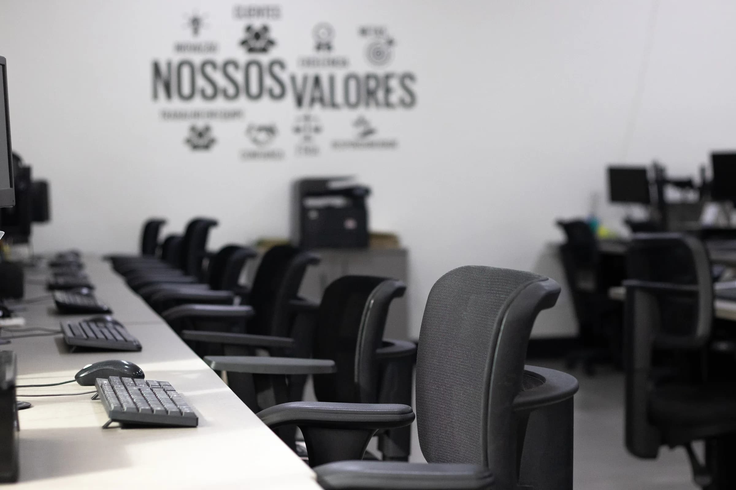 Área de trabalho da Apice, com estações lado a lado e os valores da empresa na parede.